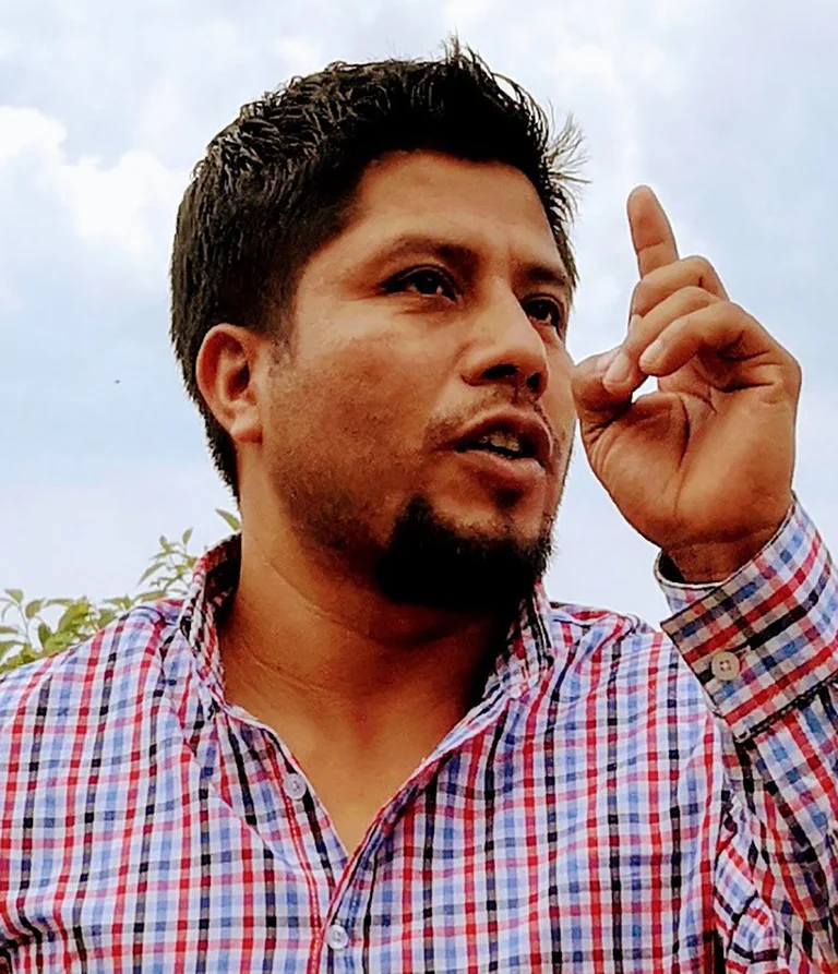 Portrait eines Mannes in kariertem Hemd. Er hat einen Zeigefinger erhoben.