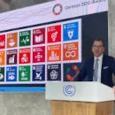 Generalsekretär Gerd Müller steht an einem Podium und redet. Hinter ihm an einer Leinwand viele bunte Kacheln.