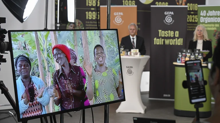 Auf einem Bildschirm l&auml;uft ein Kaffee-Videoclip, gerade sieht man Mitglieder der Kaffeegenossenschaft MEACCE, im Hintergrund ist das Podium zu sehen.