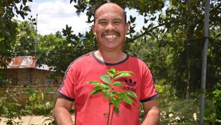 Mann h&auml;lt einen Baumsetzling und l&auml;chelt in die Kamera.