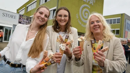 Zwei jüngere und eine ältere Frau stehen vor dem GEPA-Gebäude. Sie halten GEPA-Schokoriegel und ein Eis in der Hand und lächeln in die Kamera.
