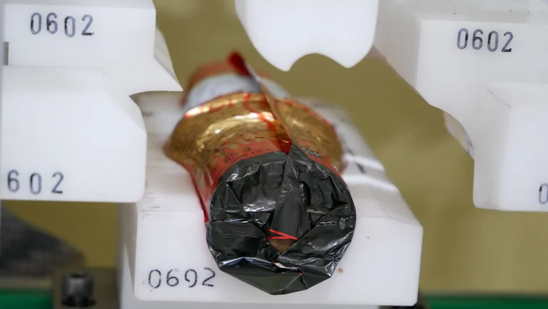 Nahaufnahme auf einen Schokonikolaus, der in eine Maschine eingelegt ist. Seine Verpackung ist noch nicht ganz verschlossen.