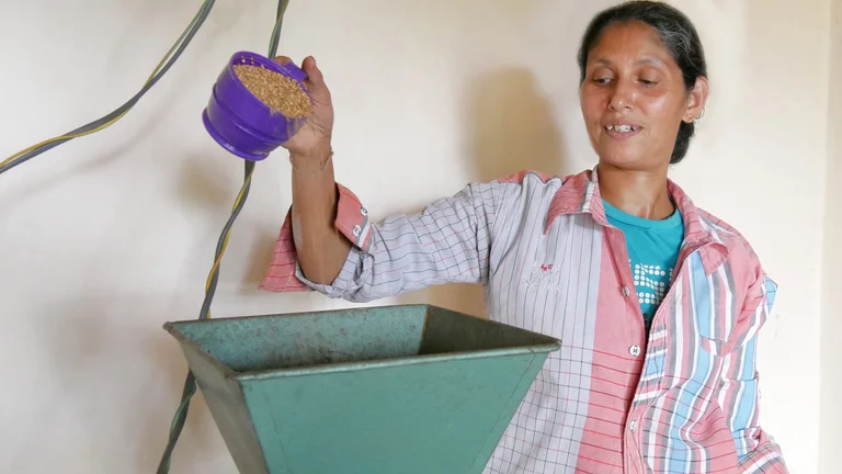 Sumithra sch&uuml;ttet K&ouml;rner in den gro&szlig;en Trichter der Gew&uuml;rzm&uuml;hle.
