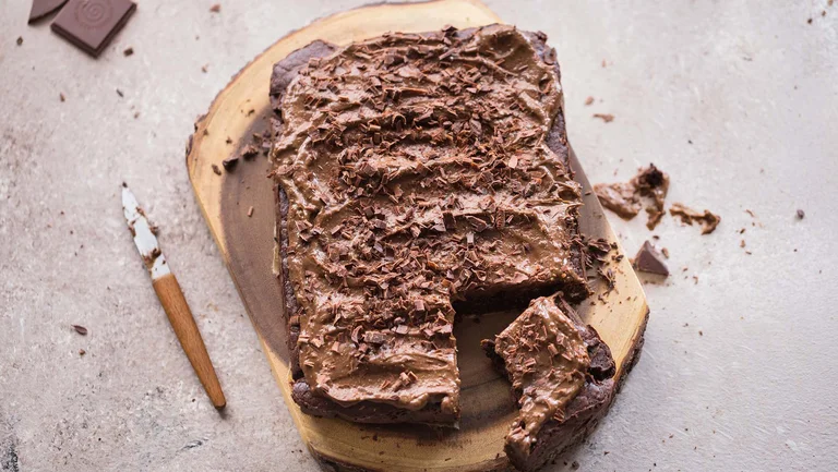 Großer Brownie auf einem Holzbrett, von dem ein Stück schon abgeschnitten ist