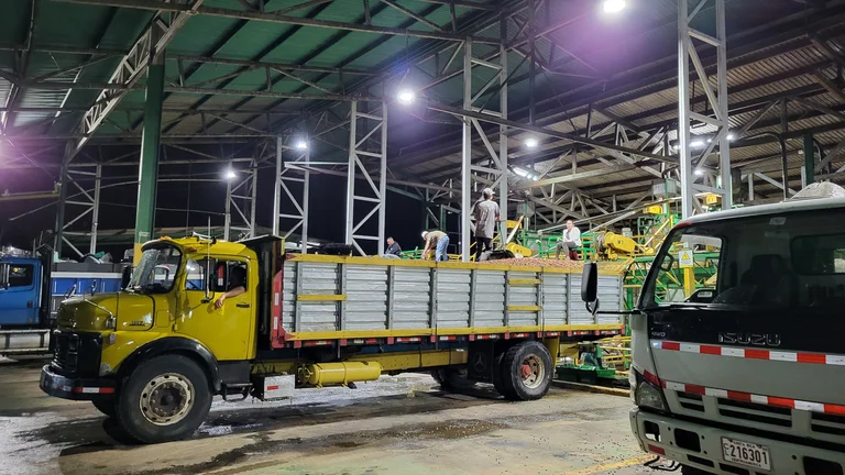 LKW an einer Verarbeitungsanlage f&uuml;r Kaffee. Es herrscht reges Treiben, obwohl es schon dunkel ist. Scheinwerfer beleuchten die Szene