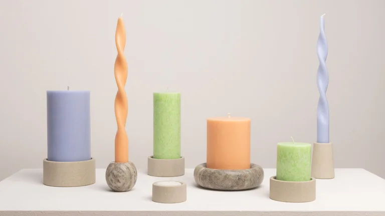 Zusammenstellung von GEPA-Kerzen in verschiedenen Formen in den Farben blasslila, pfirsich und leuchtendem hellgrün in verschiedenen Kerzenhaltern aus Palewa- oder Mintstein.