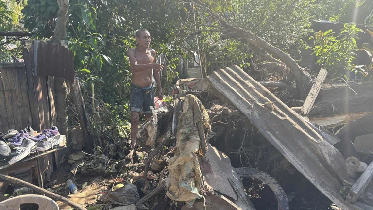 Mann in einem v&ouml;llig verw&uuml;steten Vorgarten deutet auf Tr&uuml;mmer