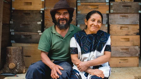Ein mexikanisches Ehepaar sitzt vor Bienenk&auml;sten und l&auml;chelt
